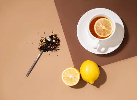 Creative flat lay of a cup of tea with lemon on a brown background with hard shadow. Food and drink concept. Top view and copy space.の写真素材