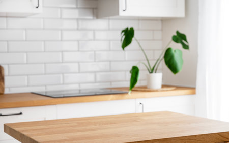 Wooden tabletop with free space for product montage or mockup against blurred white kitchen with cutting board and plant in scandinavian style in morning lightの写真素材