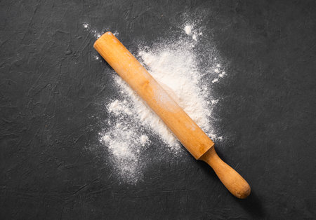 Scattered organic  flour with rolling pin on dark gray background. Homemade healthy food 
concept. Top view and copy space.の写真素材