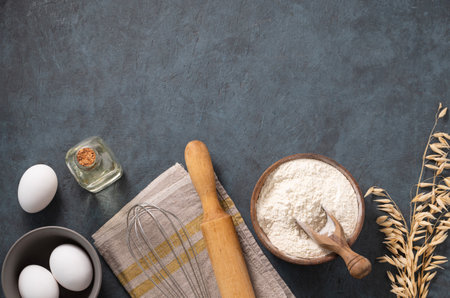Oatmeal in a wooden bowl with eggs, rolling pin and oli on a dark blue background. Natural organic flour for home baking. Top view and copy space.の写真素材
