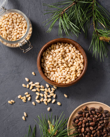 Pine nuts in a wooden bowl,  jar and scattered on a dark background with branches of pine needles. The concept of a natural, organic and healthy superfood and snack. Top view.の写真素材