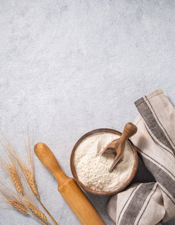 Natural flour in a wooden bowl with a scoop, rolling pin and napkin on a blue background with branches of dry wheat. Organic and healthy product for home baking. Top view and copy space.の写真素材