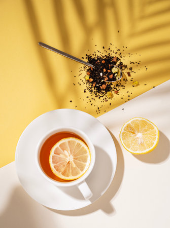 Creative summer layout of a cup of tea with lemon on a white and yellow background with a palm leaf shadow. Healthy drink concept. Top view and copy space.の写真素材