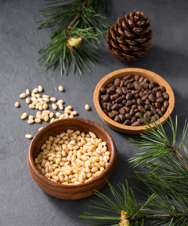 Pine nuts in a wooden bowl and scattered on a dark background with branches of pine needles. The concept of a natural, organic and healthy superfood and snack. Top view.の写真素材
