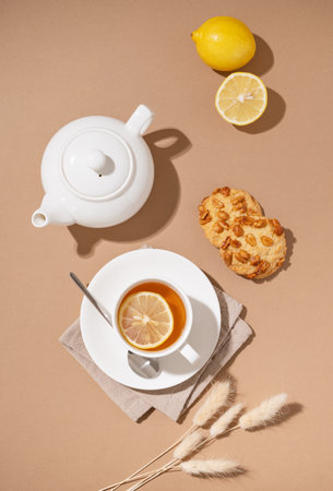 Creative layout of a cup of herbal tea with cookies, lemon and teapot on a brown background with a shadow. Healthy drink concept. Top view.の写真素材