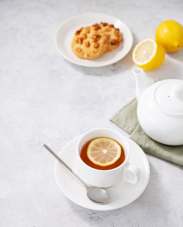 A cup of herbal tea with lemon, cookies and teapot on a light  background. Healthy and detox drink concept. Free space for text.の写真素材