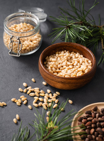 Pine nuts in a wooden bowl,  jar and scattered on a dark background with branches of pine needles close up. The concept of a natural, organic and healthy superfood and snack.の写真素材