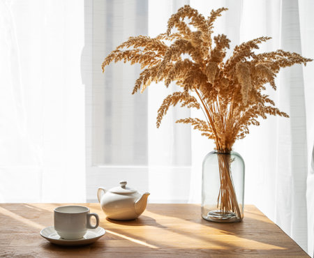 A cup of tea, teapot and dry bouquet flowers on the wooden table of a window with morning sunlight. The concept for breakfast.の写真素材