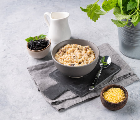 Millet porridge with prunes in a bowl on a light background with milk. The concept of a delicious and healthy breakfast. Dietary and energy food.の写真素材