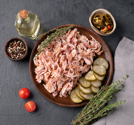Traditional barbecue torn pork or chicken meat on a wooden plate with jalapeno, pickled cucumber, fresh tomatoes and herbs on a dark background. Ingredient for burgers and sandwiches. Top view.の写真素材