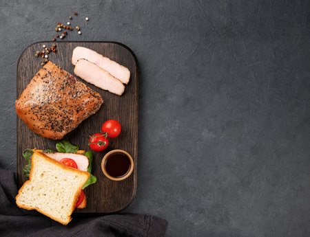 Grilled BBQ turkey breast in marinade and sandwich with fresh herbs and vegetables on a dark background. Healthy diet food. Top view and copy space.の写真素材