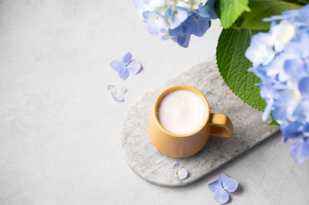 Spring bouquet with blue hydrangea flowers and a cup of cappuccino coffee in a yellow cup on a light background. The concept of a morning drink for breakfast. Top view and copy space.の写真素材