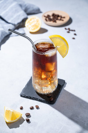 Coffee with tonic in a tall glass with ice and lemon on a light blue background with coffee beans,...