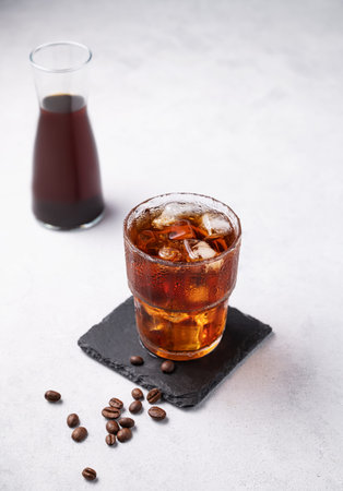Cold brew coffee in a glass with ice on a light background with coffee beans and bottle. Concept...