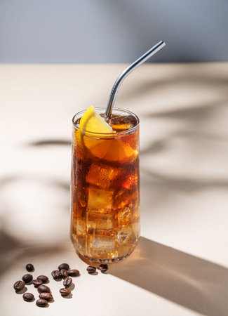 Coffee with tonic in a tall glass with ice and lemon on a yellow background with coffee beans and...
