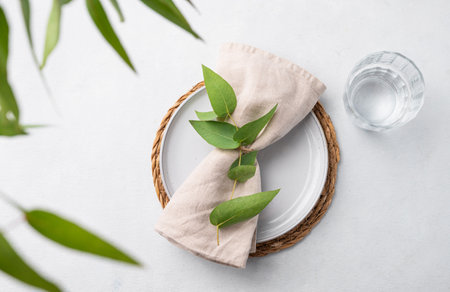 Table setting with a blue plate and a glass on a straw napkin with eucalyptus branches on a light background. Spring concept with cutlery. Top view and copy space.の写真素材