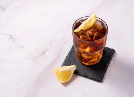 Iced tea, Cuba Libre or Long Island cocktail with cola, lemon and ice in a glass on marble...