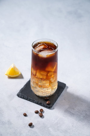 Coffee cold brew with tonic in a tall glass with ice and lemon on a light blue background with...