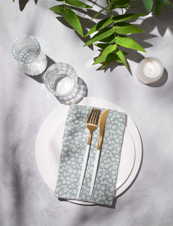 Festive table setting with white plates, glasses and candle for a celebration with eucalyptus...