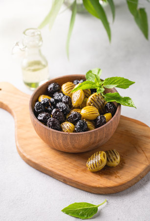 A set of green and black dried olives in wooden  bowl on a light background with olive oil and basil. The concept of vegetarian healthy snacks.の写真素材