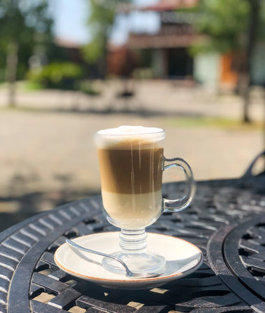 Coffee latte or cappuccino with milk foam in a tall glass on a wrought iron table in a street summer cafe.の写真素材