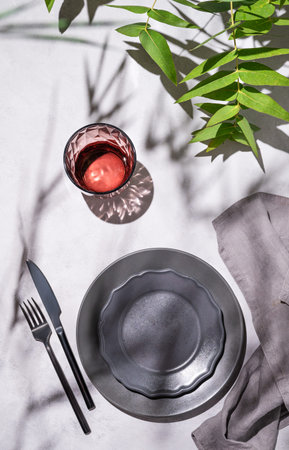 Festive table setting with dark grey plates and glass for a celebration with eucalyptus branches on...