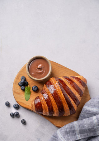 Fresh croissant with chocolate on a cutting board on a light background with a blueberries. Delicious homemade breakfast concept. Top view and copy space.の写真素材