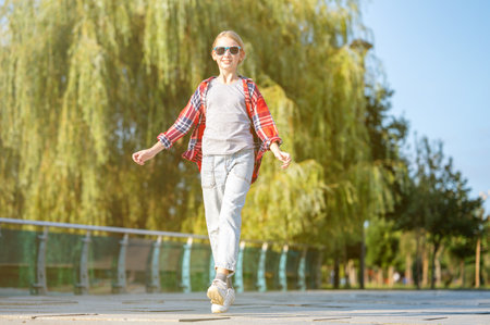A girl in a plaid shirt jumps and runs along a path in a city park on a sunny summer day. Teenage holiday concept.の写真素材