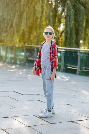 Portrait of a beautiful teenage girl in a plaid shirt and sunglasses in a city park against a background of trees on a sunny summer day.の写真素材