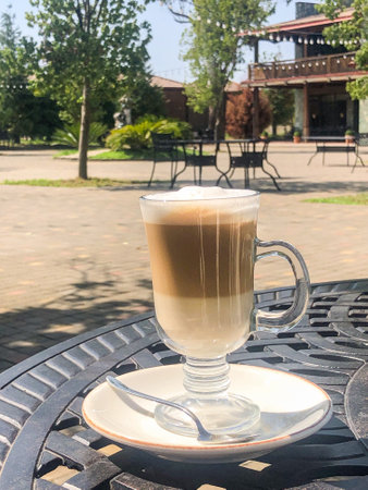 Coffee latte or cappuccino with milk foam in a tall glass on a wrought iron table in a street summer cafe.の写真素材
