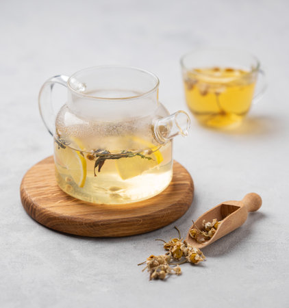 Chamomile herbal tea with lemon in a glass cup and teapot with flowers on a light background. The concept of a healthy detox drink for health and sleep.の写真素材