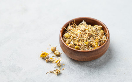 Dried chamomile in a wooden bowl on a light background. Healthy food and drink concept. Herbal  and alternative medicine with dry herbs. Free space for text.の写真素材
