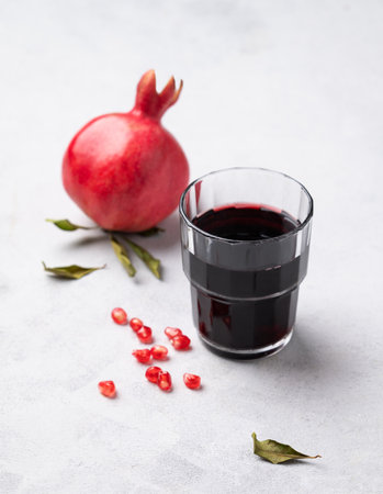 Natural pomegranate juice in a glass on a light background with fresh fruit. A healthy freshly squeezed drink with vitamins and antioxidants. Free space for text.の写真素材