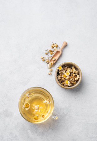 Chamomile herbal tea in a glass cup on a light background with dry flowers. The concept of a healthy detox drink for health and sleep. Top view and copy space.の写真素材