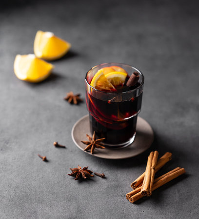 Mulled wine with orange, apple and cinnamon in glass on a dark background. The concept of a traditional winter hot drink with spices and fruits for the holiday. Free space for text.の写真素材