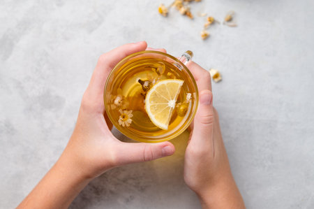 Hands holding a glass cup with chamomile herbal tea on a light background. The concept of a healthy...