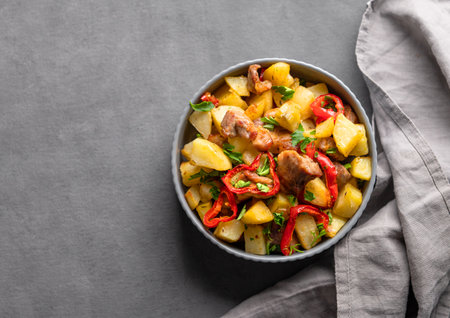 Fried pork meat with potatoes, onions and peppers. National homemade Georgian dish ojakhuri in a bowl on a dark background with napkin. Top view and copy space.の写真素材