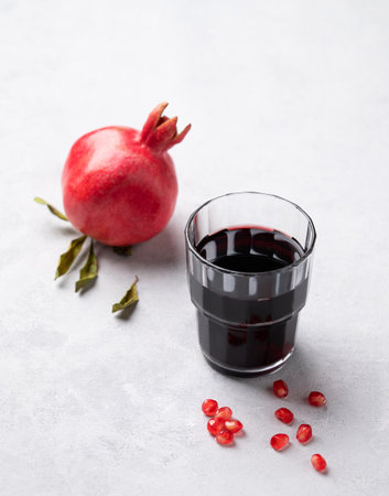 Natural pomegranate juice in a glass on a light background with fresh fruit. A healthy freshly squeezed drink with vitamins and antioxidants. Free space for text.の写真素材