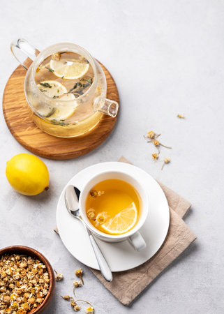 Chamomile herbal tea with lemon in a white cup and teapot with flowers on a light background. The concept of a healthy detox drink for health and sleep. Top view and copy space.の写真素材