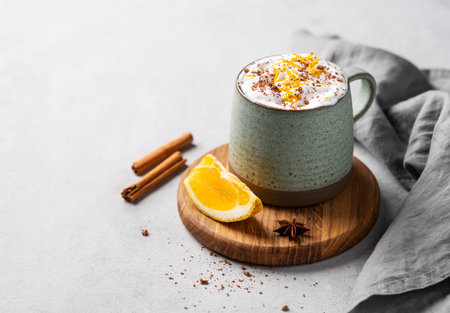 Mug of hot chocolate with whipped cream and orange zest on a wooden board on a light  background with a cinnamon sticks, napkin and fresh orange slices. Traditional winter warming drink. Copy space.の写真素材