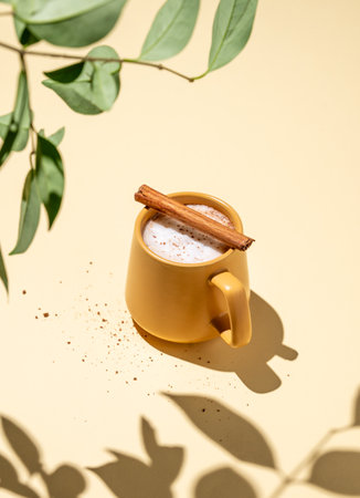 Yellow mug with foamy drink coffee latte, hot chocolate or cocoa with cinnamon sticks  on a yellow background with hard shadow and green branch. Free space for text.の写真素材