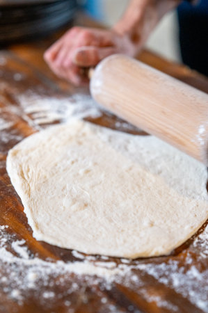 Close-up of hands rolling out dough on a dark wooden background with flour, using a rolling pin.の写真素材