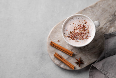White mug of hot cocoa or chocolate with whipped cream, cinnamon sticks and star anise on a gray background. The mug stands on an oval marble stand with a napkin. Top view and copy space.の写真素材