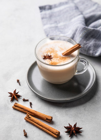 Traditional Indian masala chai latte in a glass cup. Hot drink with milk, spices and herbs on a plate on a light background with napkin.の写真素材