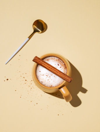 Yellow cup with foamy drink coffee latte, hot chocolate or cocoa with cinnamon sticks on a yellow background with hard shadow and spoon. Top view and copy space.の写真素材