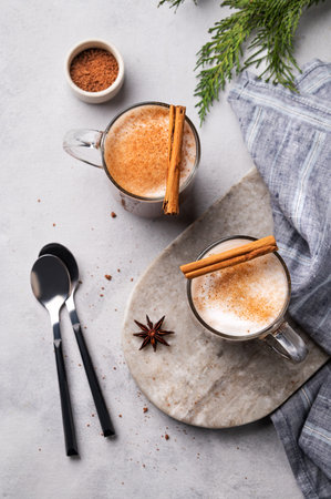 Two glass mugs with hot chocolate and milk foam on a light marble board on a gray background with cinnamon sticks, anise star and napkin. Warming winter drink concept. Top view.の写真素材