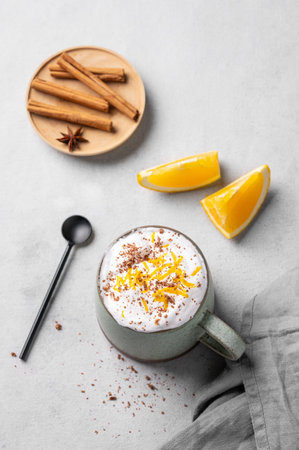 Flat lay of a mug of hot chocolate with whipped cream and orange zest on a light background with a cinnamon sticks, spoon and fresh orange slices. Traditional winter warming drink. Top view.の写真素材