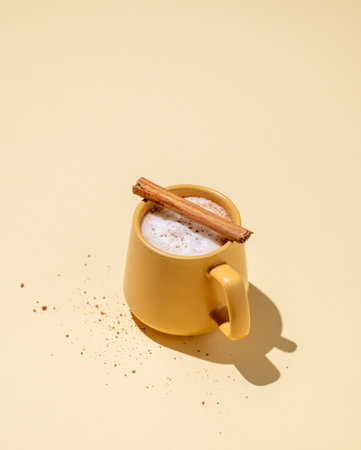 Yellow mug with foamy drink coffee latte, hot chocolate or cocoa with cinnamon sticks  on a yellow background with hard shadow. Free space for text.の写真素材