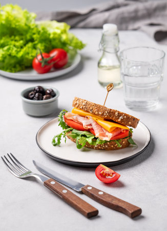 Toast club sandwich made of grain bread with cheddar cheese and bacon stuffed with tomatoes and arugula on a light background with ingredients. Healthy and dietary breakfast concept.の写真素材