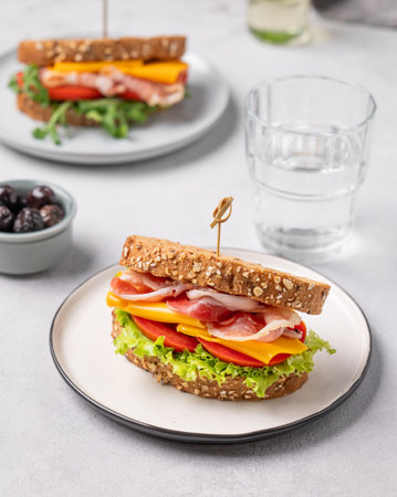 Two toast club sandwiches made of grain bread with cheddar cheese and bacon stuffed with tomatoes, lettuce on a light background with olives. Healthy and dietary breakfast concept.の写真素材